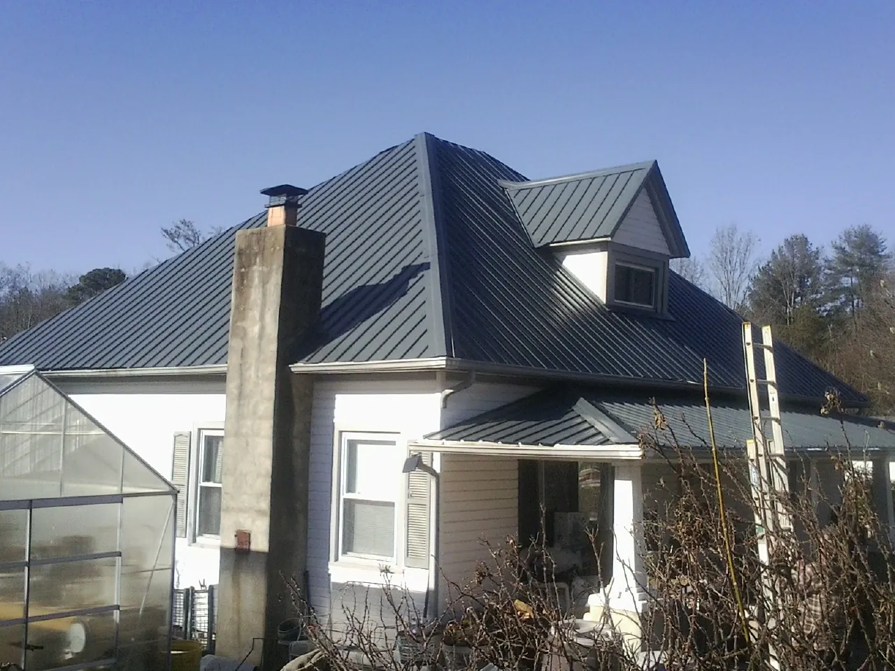 Dark blue standing seam metal roof on a white farmhouse with dormer — Slate & Tile Roof Repair by Roofing Brothers in Cope