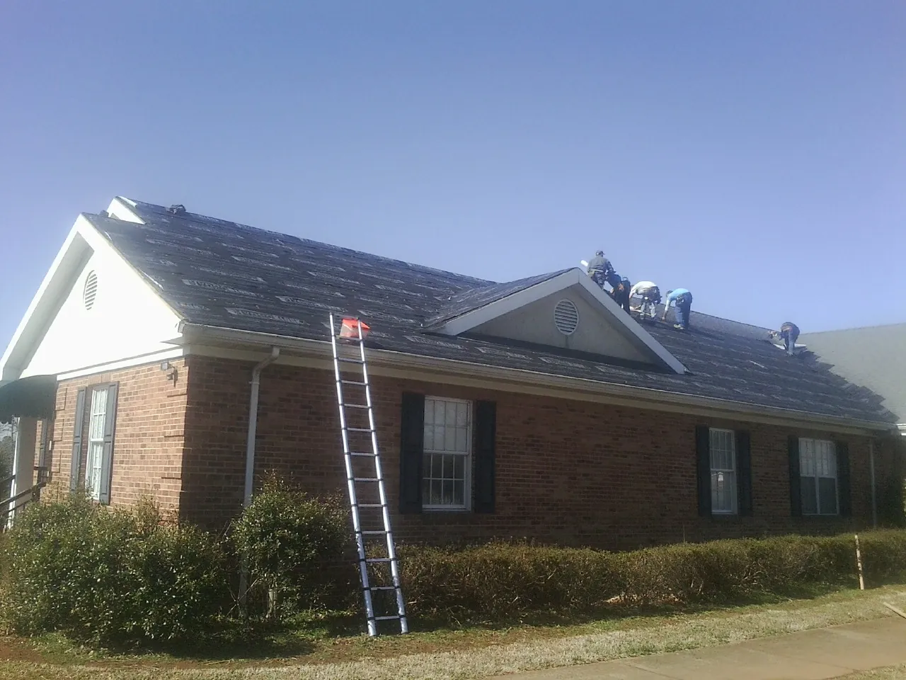 Crew tearing shingles off a brick ranch roof with a ladder set — Metal Roof Repair work by our crew in Cope
