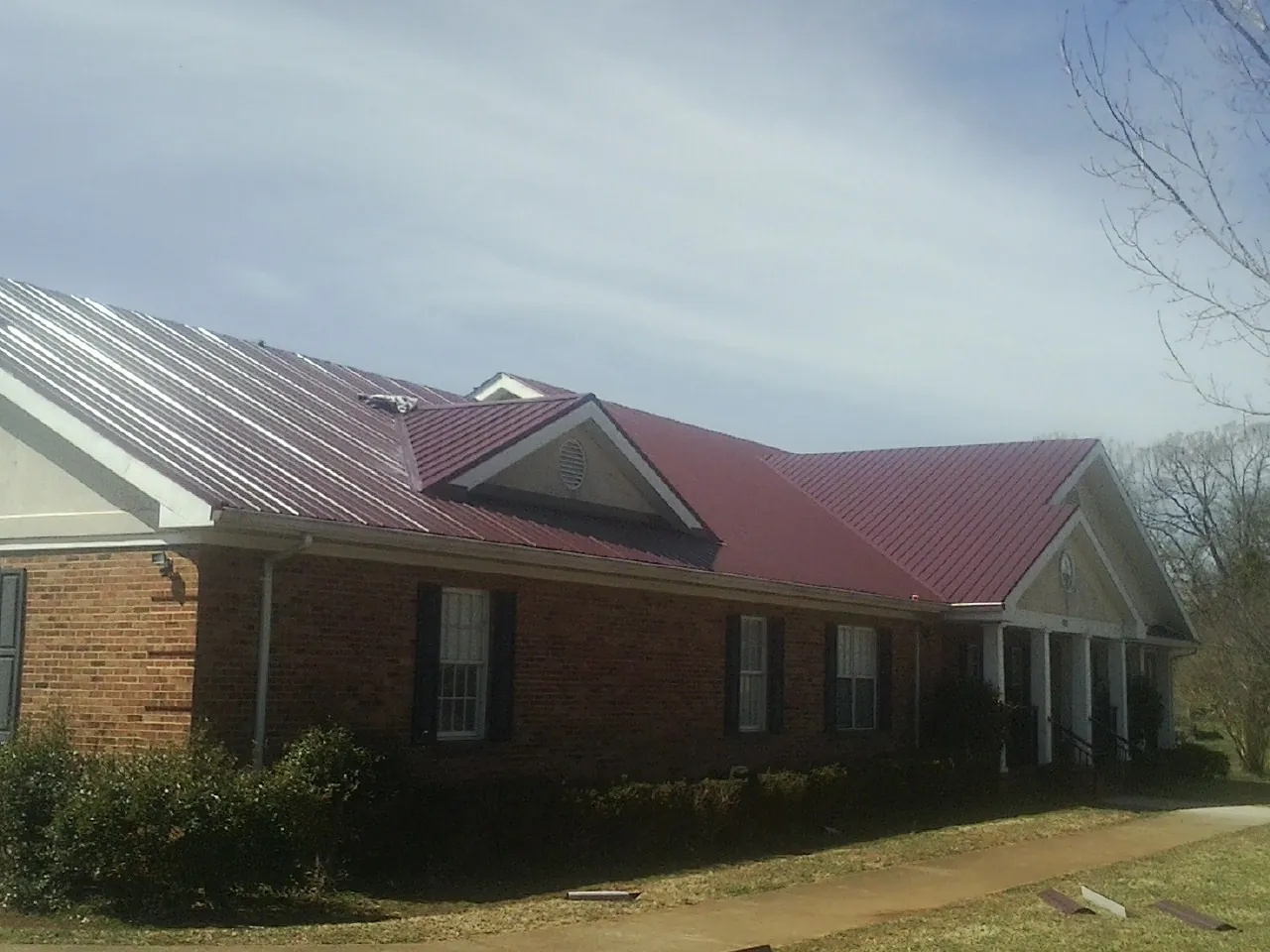 Red metal roof with gabled entries on a long brick building, from a Hail Damage Roof Repair job in Cope