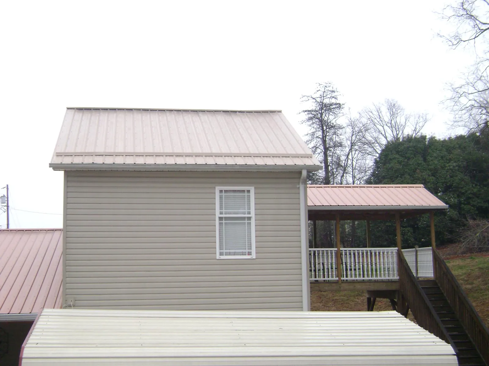 Tan metal roofs on a two story addition and attached porch, from a Roof Replacement job in Cope
